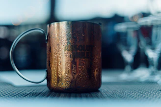 A copper glass being held by a person, with droplets of water on its surface.