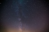 An expansive night sky filled with countless stars, dominated by the Milky Way galaxy stretching vertically across the image. The stars vary in brightness against the dark backdrop.