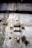 A weathered and deteriorating industrial wall features peeling paint, rust spots, and exposed metal rods. There is a black cable running vertically across the surface, and visible patches of mold or mildew contribute a sense of decay.