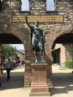 A detailed Roman legionnaire in full armor standing guard at the military camp entrance at dawn.