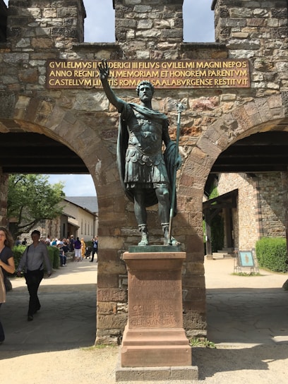 A detailed Roman legionnaire in full armor standing guard at the military camp entrance at dawn.