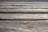 A close-up view of an aged wooden surface with visible grain patterns and knots. The boards are aligned parallel, creating a textured and natural appearance.