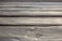 A close-up view of an aged wooden surface with visible grain patterns and knots. The boards are aligned parallel, creating a textured and natural appearance.