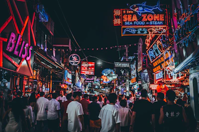 City street at night illuminated by colorful neon signs and bustling crowds.