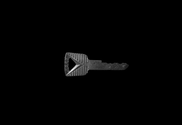 A single metallic key on a black background, featuring a rectangular head with textured grooves and a triangular cutout.