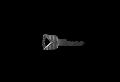 A single metallic key on a black background, featuring a rectangular head with textured grooves and a triangular cutout.