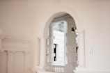 An elegant interior featuring white classical architecture with arches, columns, and decorative moldings. Soft lighting casts subtle shadows, enhancing the refined and minimalistic aesthetic.