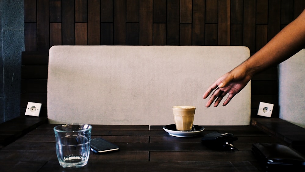 Person, die versucht, eine braune Tasse zu greifen