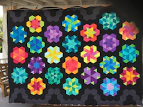 An art quilt featuring intricate patterns and bold color contrasts hanging on a wooden wall.