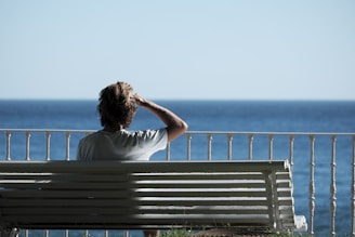 man sitting on bench near body of water during daytime