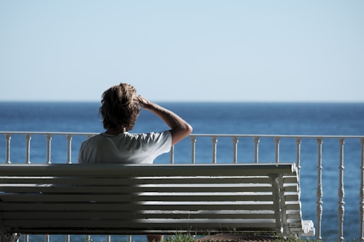 man sitting on bench near body of water during daytime