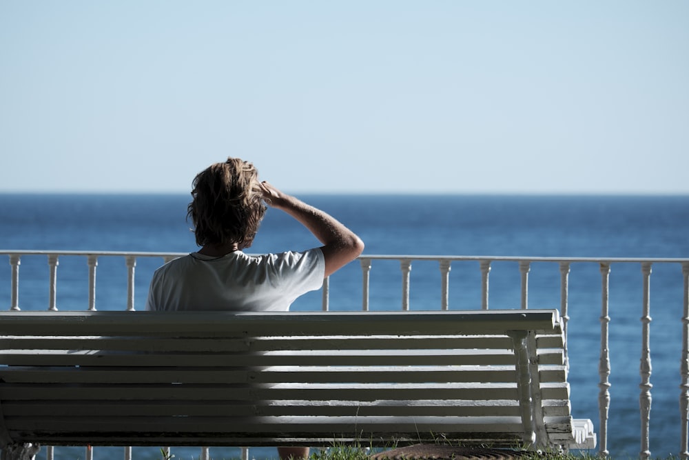 man sitting on bench near body of water during daytime