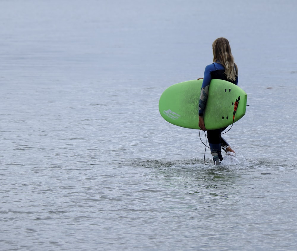 woman walking on body of water carrying green surfboard during daytime