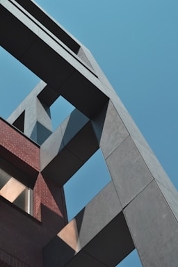 A modern architectural design with intersecting geometric structures made of concrete and brick. The building is framed against a clear blue sky, with light creating shadows on the surfaces.