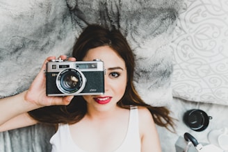 A warm portrait of Jolanta Loseva holding her camera, smiling gently in a sunlit studio filled with photo prints.