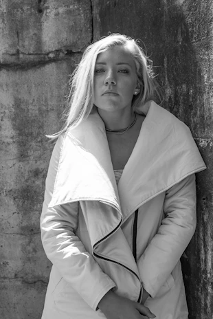 Structured coat draped over a simple dress against a muted urban backdrop.