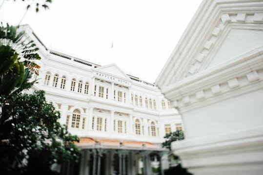 A grand colonial-style hotel with an ornate facade and arched windows is surrounded by lush greenery. The architecture features intricate details and a classic design, giving it an elegant appearance.