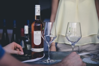 person holding clear wine glass sitting opposite woman on date, with a wine bottle on the table