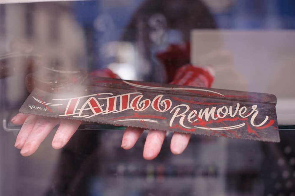 person holding brown wooden Tattoo remover sign