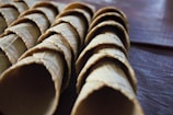 A row of colorful ice cream cones lined up on a rustic wooden table.