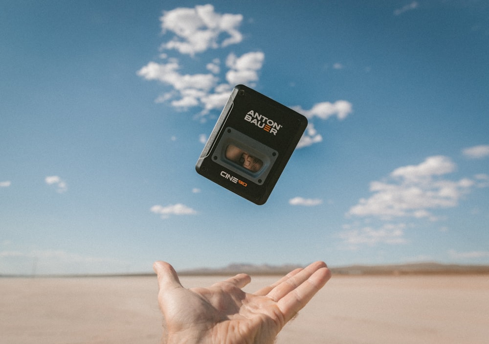 person catching black Anton Bauer device under blue sky during daytime