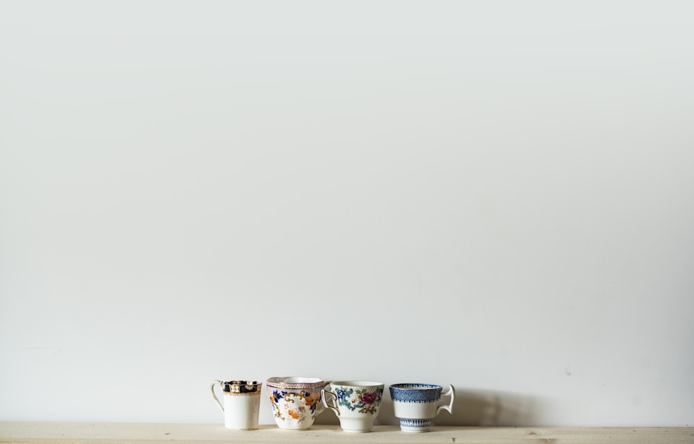 Cuatro tazas de cerámica de colores variados sobre mesa blanca