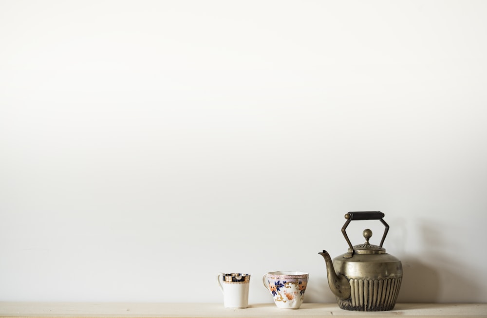 silver kettle beside two mugs