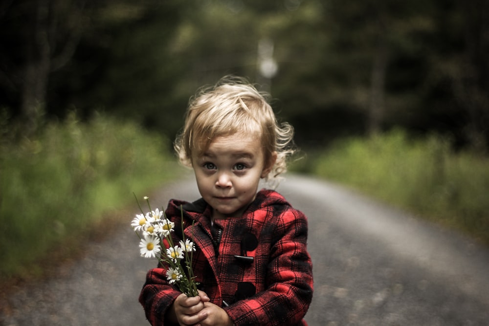 girl wearing red and black plaid jacket holding flower