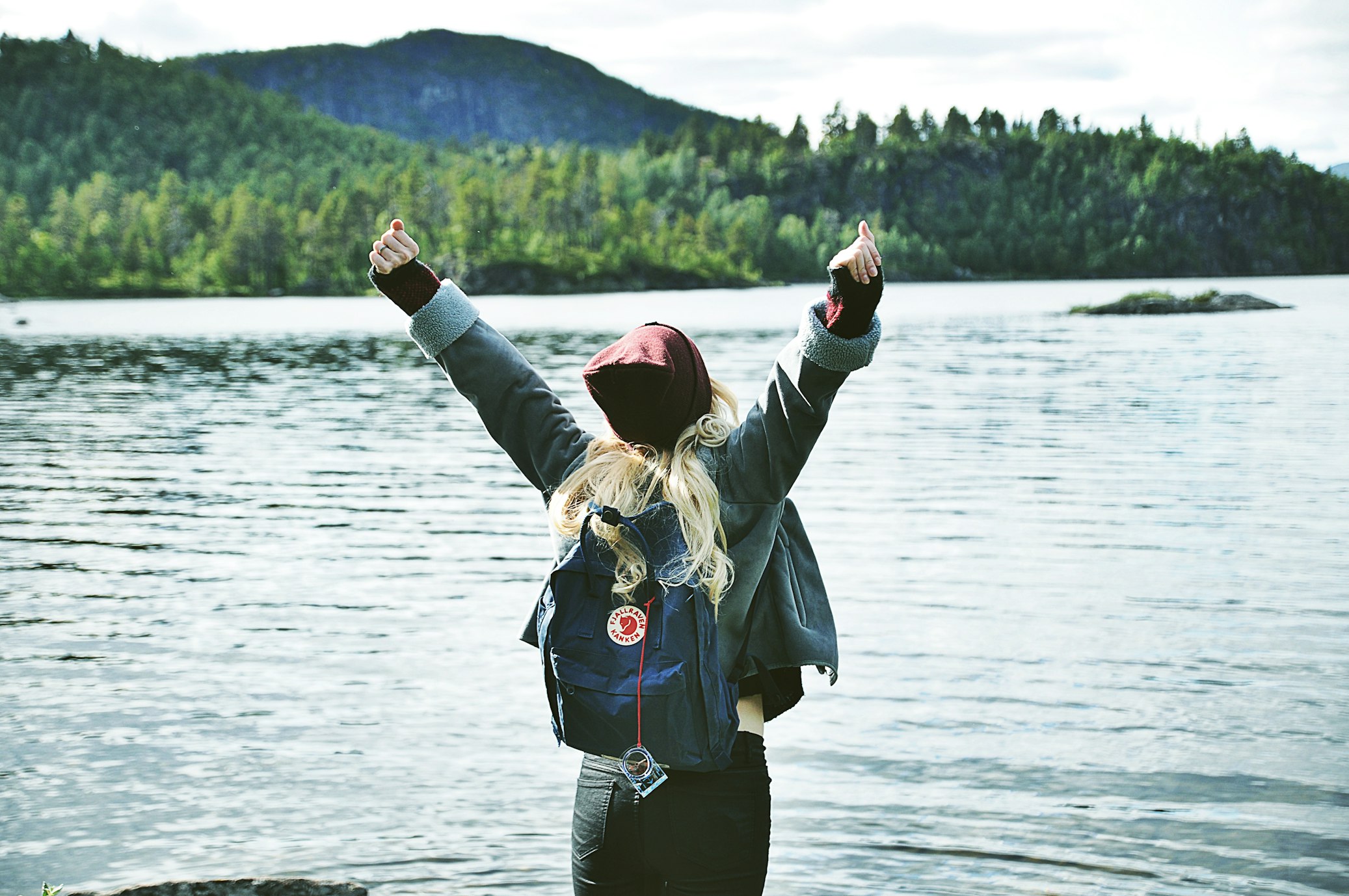 Woman stands in front of a lake with her arms up in celebration. Self confidence quotes blog by Inspired Idiots
