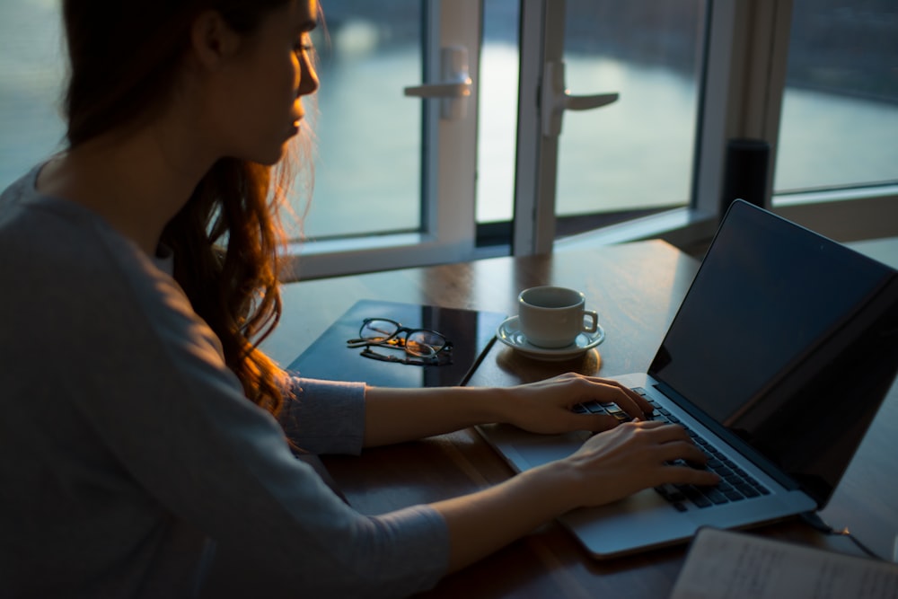 Mulher dona de uma Sociedade Limitada Unipessoal (SLU) sentada ao lado da mesa, digitando em seu laptop.