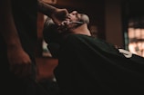 man sitting on barber's chair getting his beard trimmed by a scissor