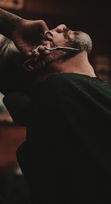 man sitting on barber's chair getting his beard trimmed by a scissor