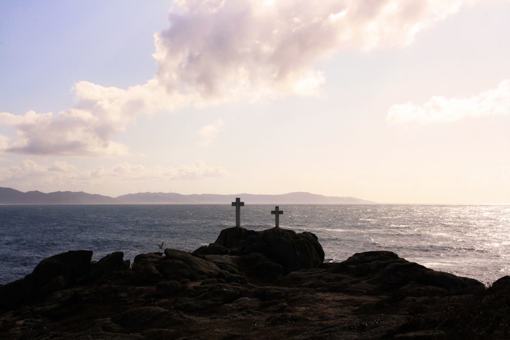 Two little wooden crosses sitting on top of a rock cliff near an ocean.