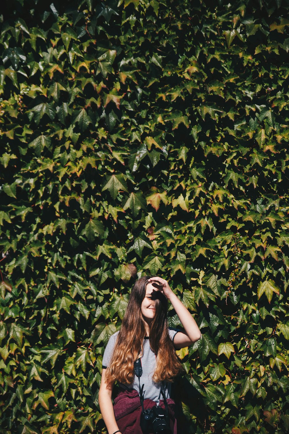 A long-haired woman standing in front of a large tree.