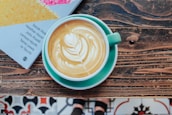 Close-up of a coffee cup with latte art resting on a neutral-toned table next to a vintage book.