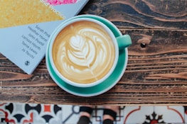 Close-up of a coffee cup with latte art resting on a neutral-toned table next to a vintage book.