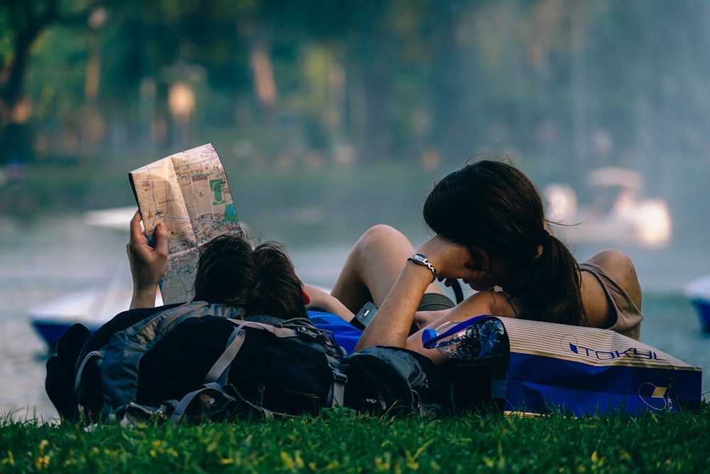 Man and woman lying down in field on bags while looking at a map