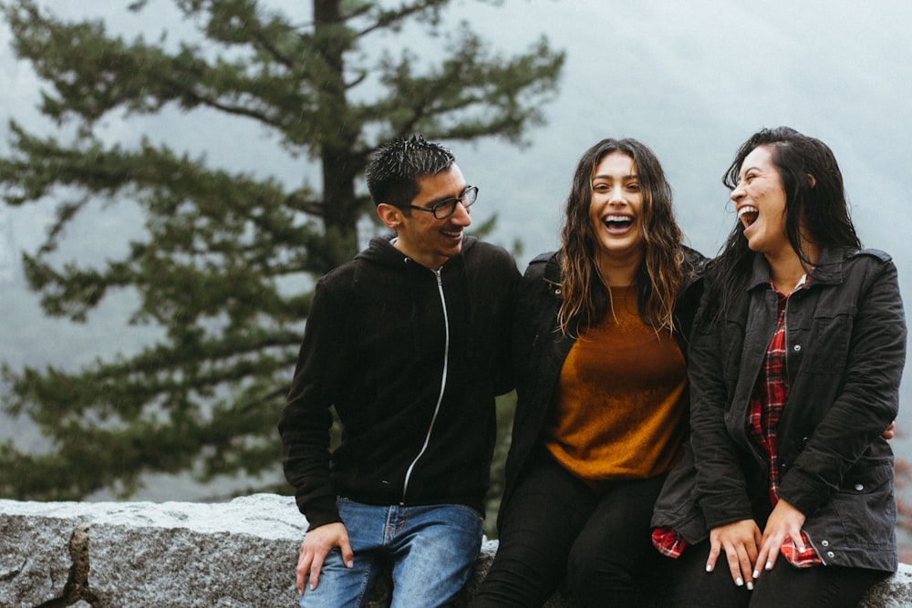 man sitting beside two woman on gray surface