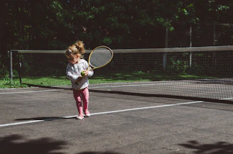 girl holding lawn tennis racket while standing beside white and black net
