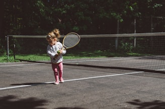 girl holding lawn tennis racket while standing beside white and black net