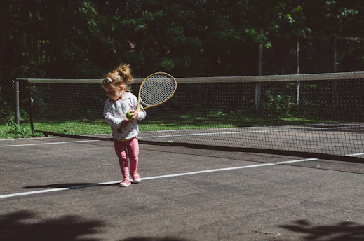girl holding lawn tennis racket while standing beside white and black net