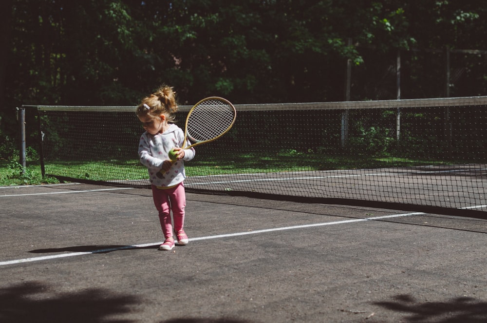 잔디 테니스 라켓을 들고 흰색과 검은 색 그물 옆에 서있는 소녀
