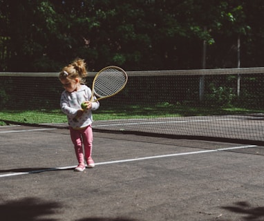 girl holding lawn tennis racket while standing beside white and black net