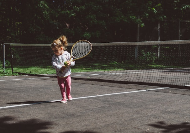 girl holding lawn tennis racket while standing beside white and black net