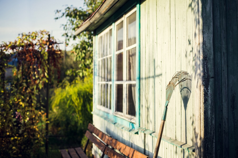 garden rake leaning on white wooden wall at daytime