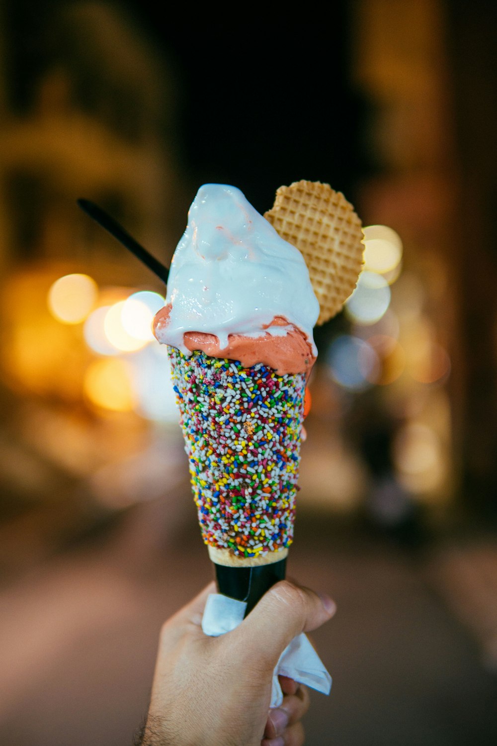 person holding multicolored sprinkled ice cream cone with vanilla flavored ice cream