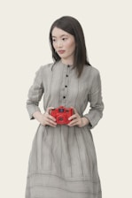 woman wearing gray striped button-up long-sleeved dress holding red point-and-shoot camera