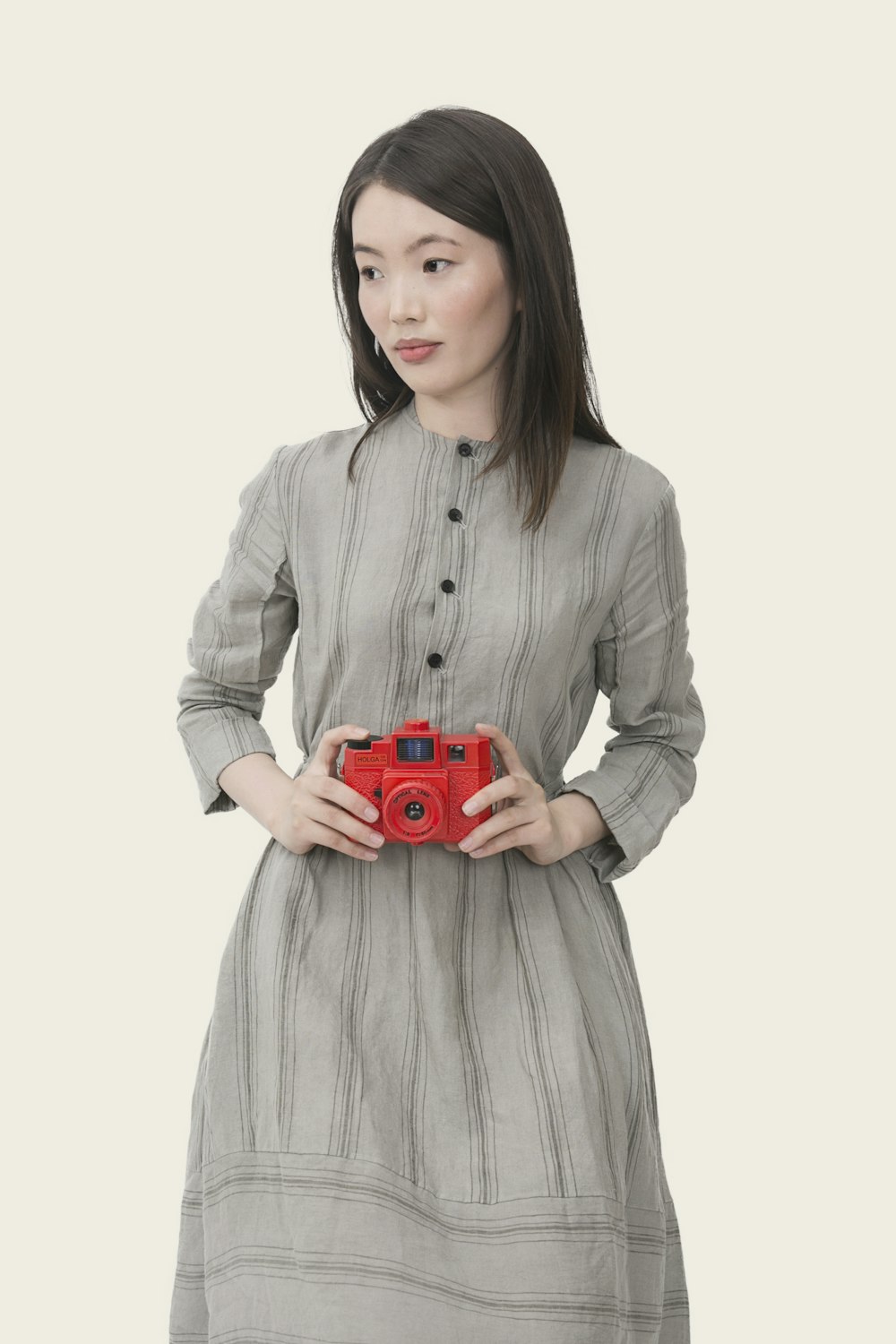 mujer con vestido de manga larga con botones a rayas grises sosteniendo una cámara roja de apuntar y disparar