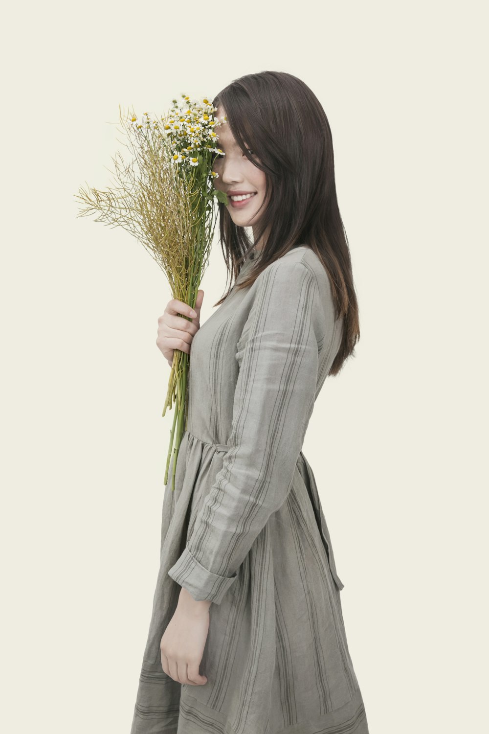 灰色と黒の縞模様の長袖ドレスを着て、白い花びらの花を手にした女性
