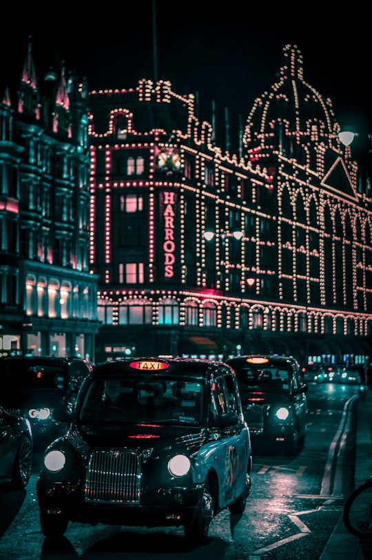 black taxi in the street passing trough Harrods Mall during nighttime in Hyde Park United Kingdom